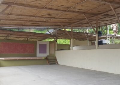 Área recreativa cubierta del complejo Don Omar con estructura de madera, piso de hormigón y paredes parcialmente pintadas.